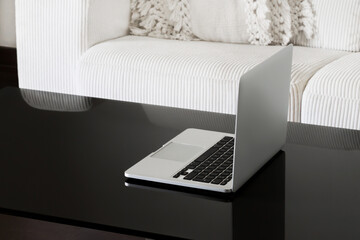 Canvas Print - Laptop on a black glass table against a white sofa. Back view. The screen is not visible.