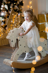 Merry Christmas and happy New year! Portrait of a little one-year-old girl on a toy horse in the living room. Concept of children's holidays and family.