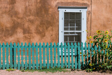 Sunflowers And Turquoise Color Wood Fence Set In Front Of A Window And Old Adobe Wall Along Canyon Road In Santa Fe, New Mexico