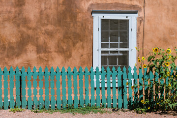 Sunflowers and turquoise color wood fence set in front of a window and old adobe wall along Canyon Road in Santa Fe, New Mexico