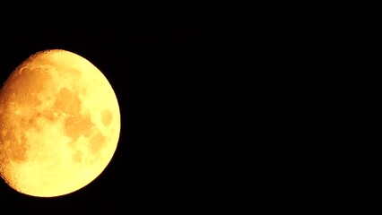 Wall Mural - A glowing golden huge moon seen from earth through the atmosphere against a starry night sky. A large moon moves across the sky, the moon moving from the left frame to the right.