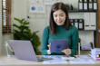 © ArLawKa - Asian businesswoman working on financial paperwork using laptop online tax, loan, bank debt for mathematical finance on desk, accounting, statistics and analytical research concept.