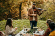 A handsome man plays the violin at a small wedding party while people are eating, clapping, and listening to his music.