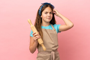 Sticker - Little caucasian girl holding a rolling pin isolated on pink background having doubts