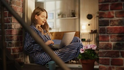 Wall Mural - Female Manager Writing her Work Emails Using a Laptop While Sitting on her Windowsill. Young Beautiful Woman Enjoying Calmness and Comfort Thanks to Possibility to do a Remote Job