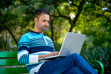 Young indian man working on laptop at park.