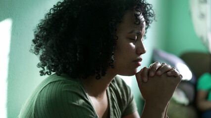 Wall Mural - A hopeful Brazilian young woman praying at home. An African South American person having FAITH