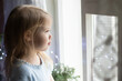 © Оксана Рязанова - bored cute little girl looking out of window on background sparkle blurred lights at home