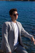 © Beatriz - Hombre caucásico de mediana edad moreno con traje y gafas de sol esperando a su cita para San Valentín con el tranquilo mar Mediterráneo de fondo.