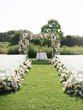 Countryside wedding ceremony with arch, decorated with flowers and guests chairs, placed on green meadow at sunny day
