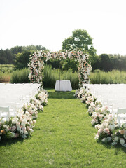 Wall Mural - Countryside wedding ceremony with arch, decorated with flowers and guests chairs, placed on green meadow at sunny day