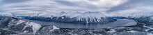 Panoramic Aerial Image Of Tutshi Lake On A Grey Day With Dramatic Clouds With Snow Capped Mountains In Winter; Yukon, Canada