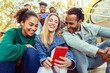 © Xavier Lorenzo - United group of international friends laughing together watching social media content on mobile phone app. Diverse millennial young adult people laughing together while taking vertical selfie portrait