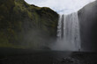 A person walking away from the imposing Skógafoss waterfall in southwestern Iceland.