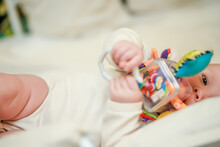 A newborn baby lies on her side and holds an educational toy in her hands. Toy for tactile sensations and the study of shapes and colors of toddlers