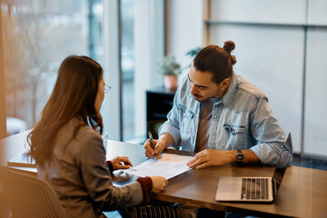 Wall Mural - Young Hispanic man signing loan agreement during meeting with his bank manager in office.