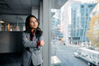 © Drazen - Asian businesswoman with arms crossed looking through window in office.