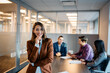 © Drazen - Happy female CEO in front of her business team in office looking at camera.