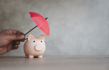 Finance insurance and safe investment concept. Hand hold small red umbrella over piggy bank protect money