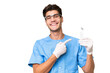 © luismolinero - Young dentist man holding tools over isolated background pointing to the side to present a product