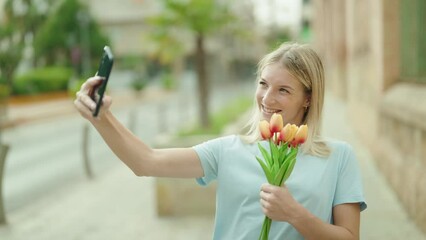 Wall Mural - Young blonde woman make selfie by smartphone holding bouquet of flowers at street