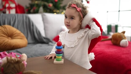 Sticker - Adorable caucasian girl playing with toy standing by christmas tree at home