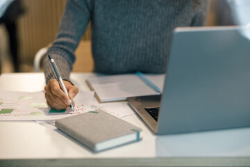 Wall Mural - Close up of woman freelancer working laptop and making notes while sitting near windows in cozy cafe