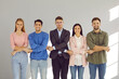 © Studio Romantic - Portrait of team of young positive men and women holding hands looking at camera. Happy corporate employees standing in row on gray wall background with sunlight. Concept of friendship and unity.