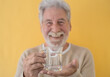 © luciano - Defocused attractive bearded senior man holding a glass of fresh water looking at camera standing on yellow background