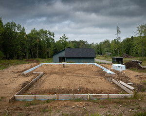 Poster - New house construction job site in a home development, with wood forms in place for concrete cement to be poured for the floor.