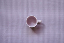 Empty Mug Cup On Purple Check Pattern Fabric Background. Top View