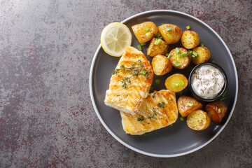 Wall Mural - Grilled fish cod fillet with thyme served with baked potatoes, cream sauce and lemon on the table. Horizontal top view from above