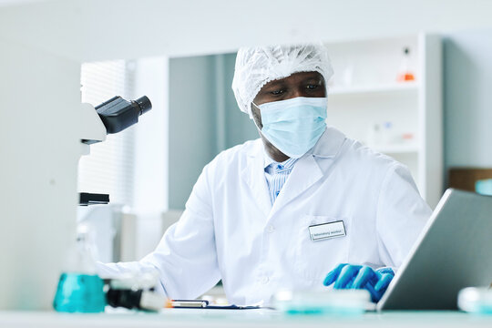 Portrait of black man doing scientific research in laboratory and wearing face mask