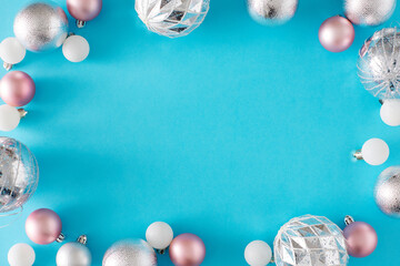 Wall Mural - Christmas decorations concept. Flat lay holiday composition of pink and white christmas baubles on pastel blue background with copy space in the middle.