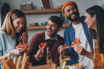 Wall Mural - Cheerful young people eating pizza and laughing while enjoying fun time together