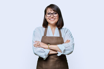 Confident middle aged woman in apron looking at camera on white background