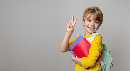 Primary school smiling boy girl over grey background with backpack and colorful exercise book showing thumbs up. Copy space for advertising blank concept. Back to school. Childhood, education