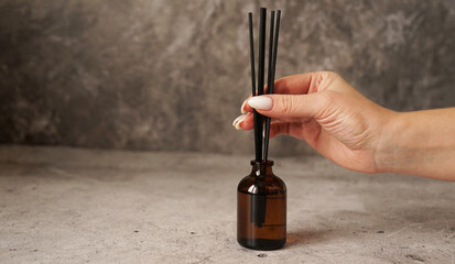 aromatic reed diffuser bottle with black sticks on a dark marble background. womans hand holding dif