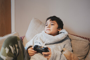 Wall Mural - Kid playing video game in living room,Lifestyle portrait of young boy playing game online holding controller having fun sitting on sofa,Happy Child in gamer emotion holding joystick play alone at home