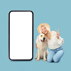 Happy woman sitting near her labrador dog and showing peace gesture, posing near big cellphone with empty screen