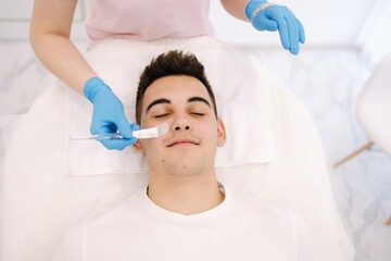 Young brunette hair man during peeling treatment in beauty clinic. Handsome man in cosmetology studio