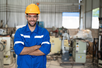 Wall Mural - Portrait of male engineer in uniform smiling arms crossed at industrial factory. Technician man standing wearing yellow helmet safety in manufacturing workshop.