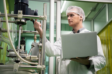 Apothecary scientist using laptop to record information from a CBD oil extractor and a scientific machine used to create medicinal cannabis products.