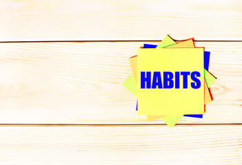 Wall Mural - Multicolored office paper stickers with the text HABITS on a wooden background. copy space