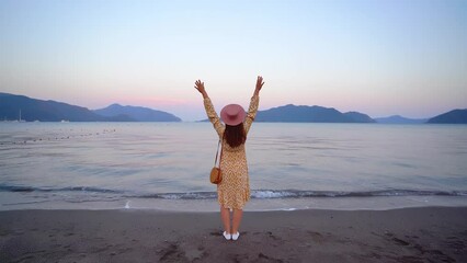 Wall Mural - Back of alone traveler woman standing alone with open arms at sunset by the sea. Inspired female enjoying happiness, traveling and free life moment