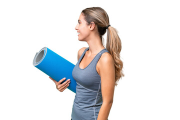 Canvas Print - Pretty Young Uruguayan sport woman going to yoga classes while holding a mat over isolated background laughing in lateral position