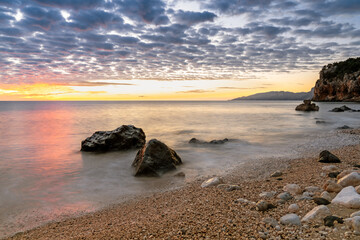 Sticker - colorful sunrise at Cala Gonone beach with black and white rocks and boulders in the foreground