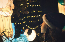 A Little Girl Wearing A Warm Winter Hat Looking Up At An Illuminated Christmas Decoration