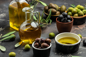 Olive oil in two glass containers and harvest olives berries in bowls on a dark background