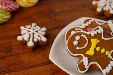 Wall Mural - Two gingerbread men with colorful icing on a white dessert plate on a wooden table with gingerbread and caramels in the background.